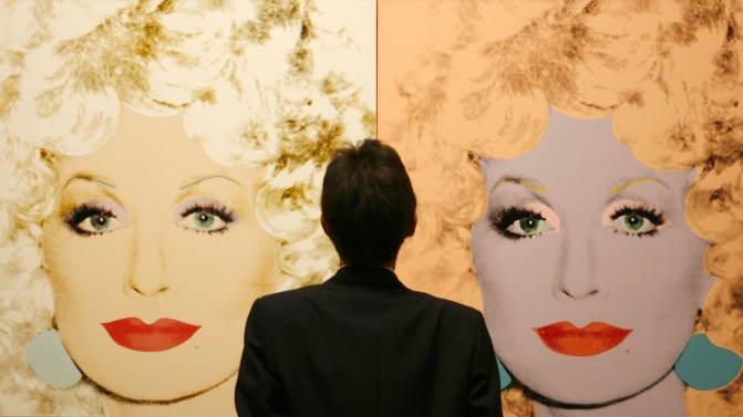 A gallery attendant stands in front of canvas prints of singer and actress Dolly Parton during the setting up of an Andy Warhol exhibtion in the National Gallery Complex in Edinburgh, Scotland