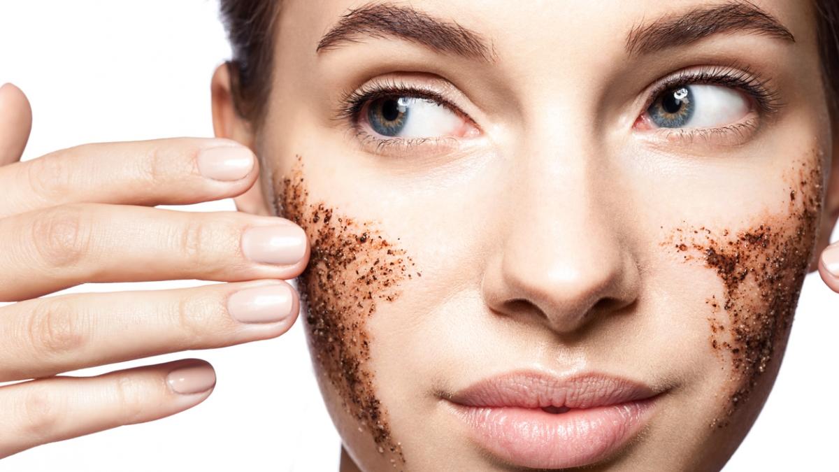 Close-up portrait of a beautiful woman with a coffee scrub on her face doing peeling skin isolated on white background