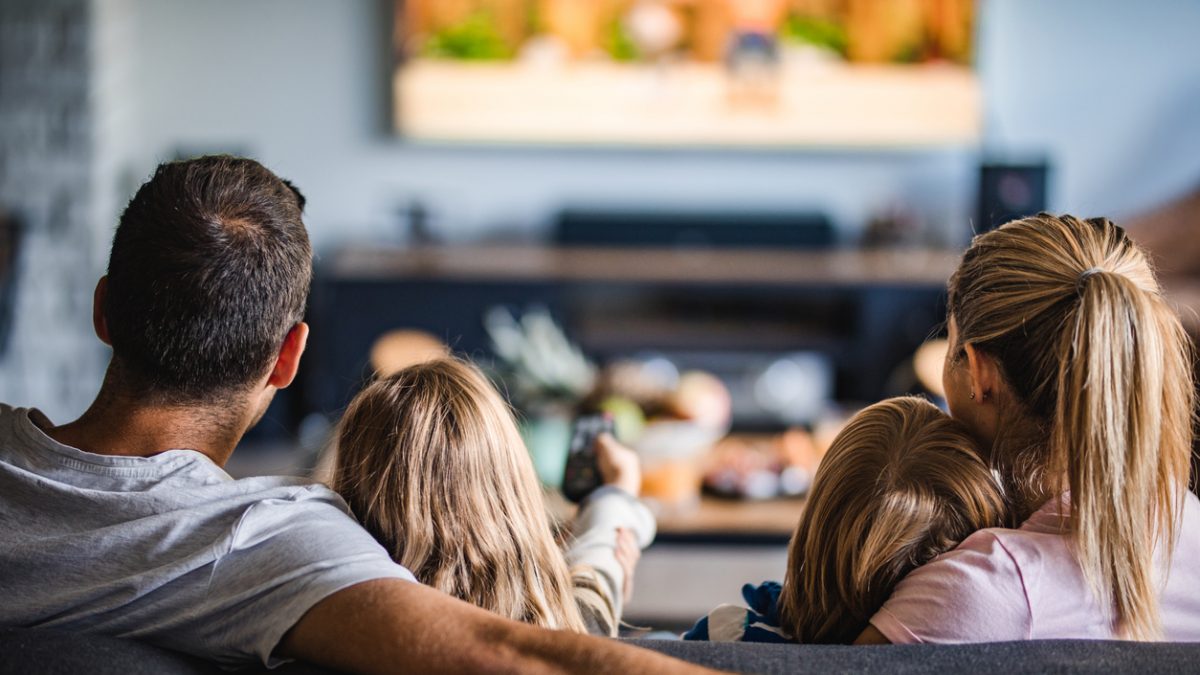 Rear view of a family watching TV on sofa at home.