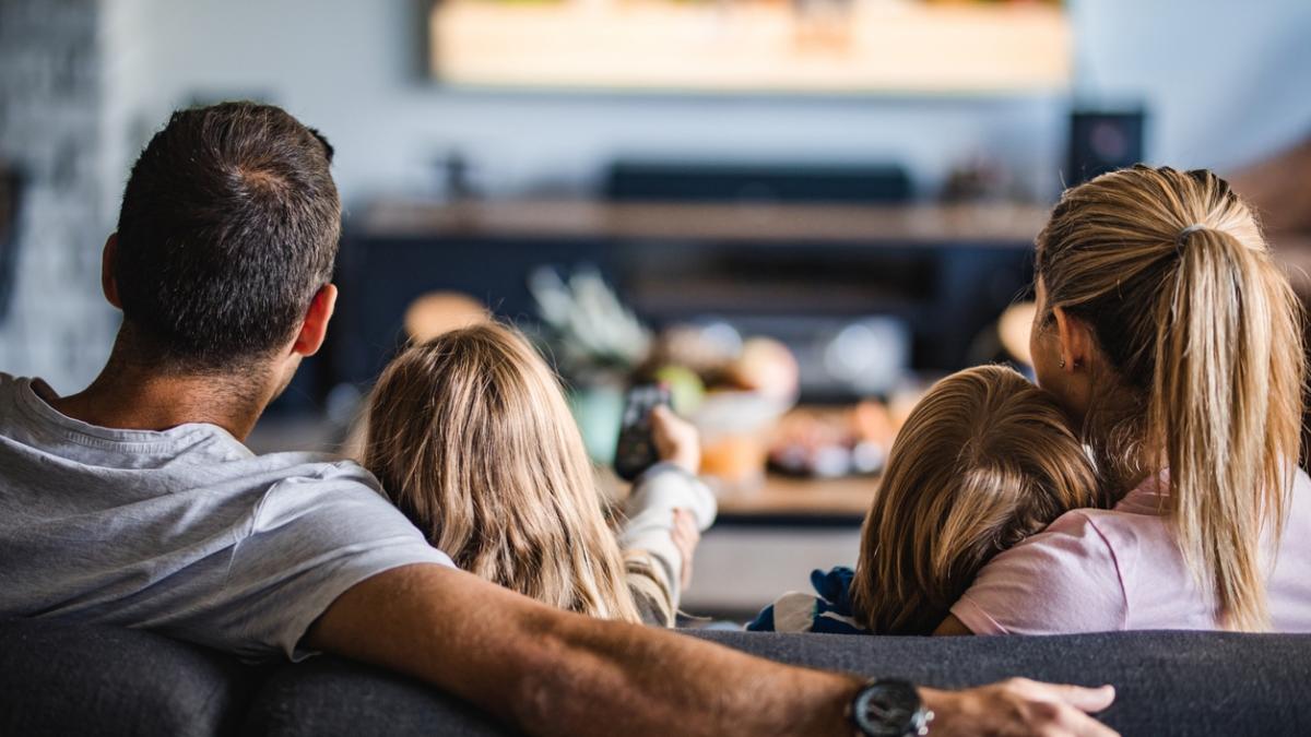 Rear view of a family watching TV on sofa at home.