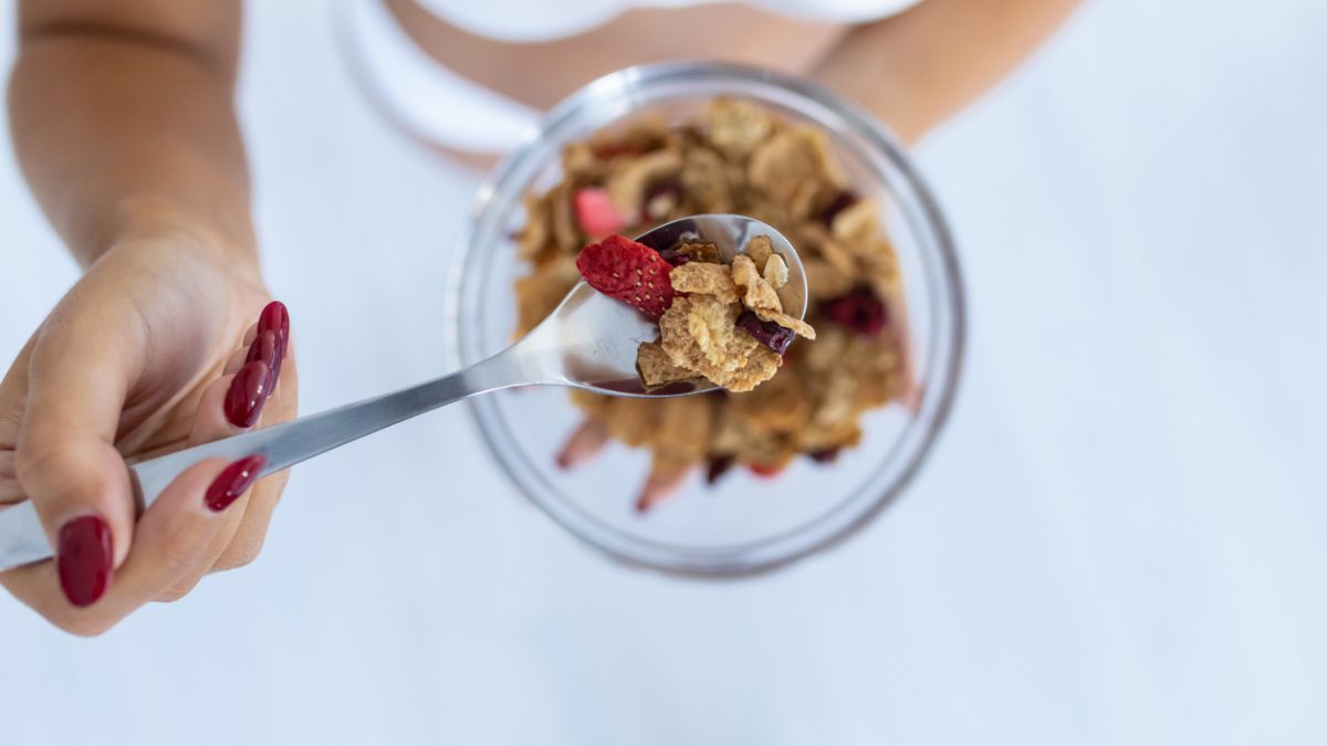 Hands of young woman holding bowl with breakfast cereals at home.
