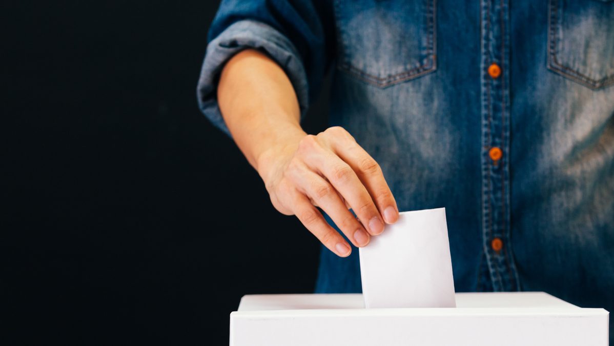 Front view of person holding ballot paper casting vote at a polling station for election vote in black background