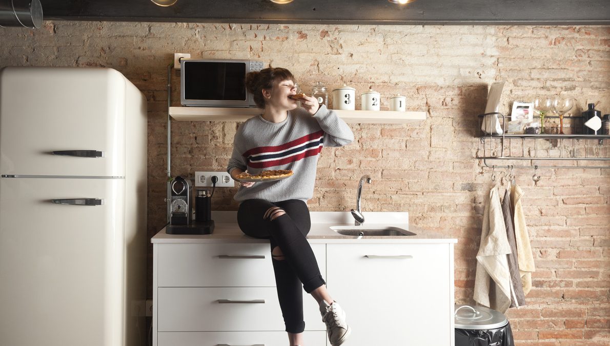 Beautiful girl eating pizza in a modern kitchen
