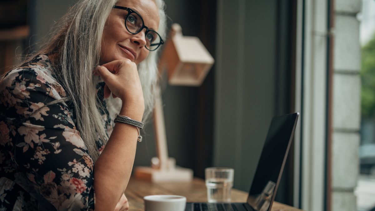 Beautiful senior woman working on laptop while drinking coffee