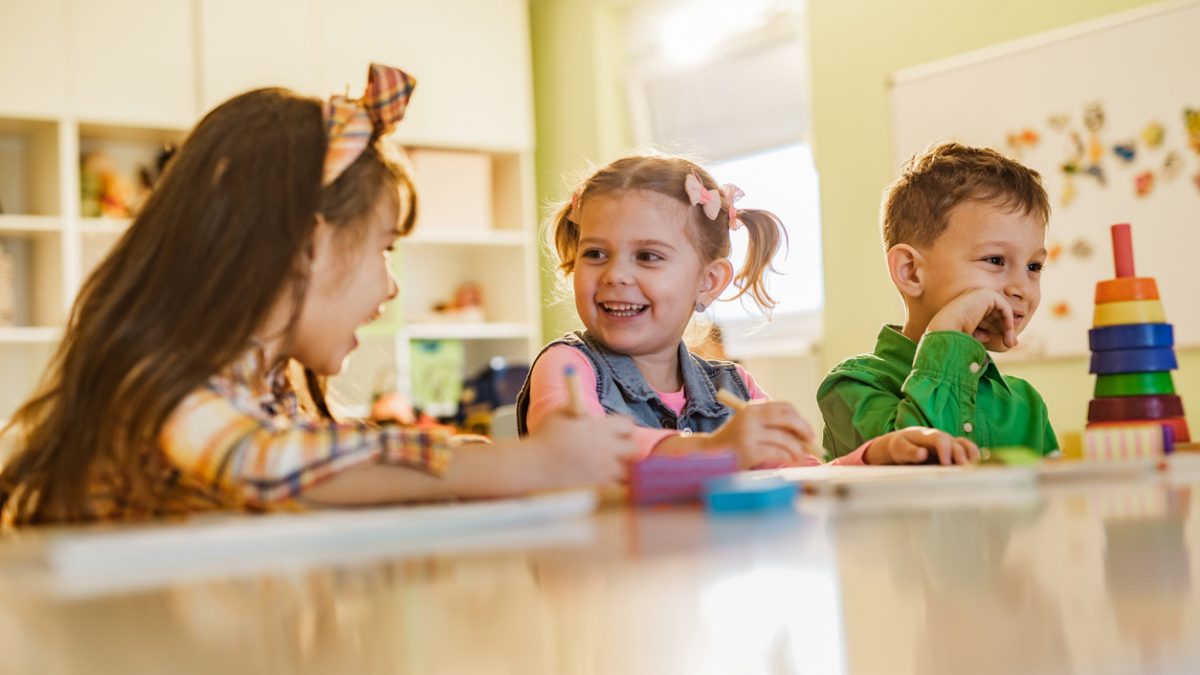 Smiling little girl and her friends sketching at preschool.