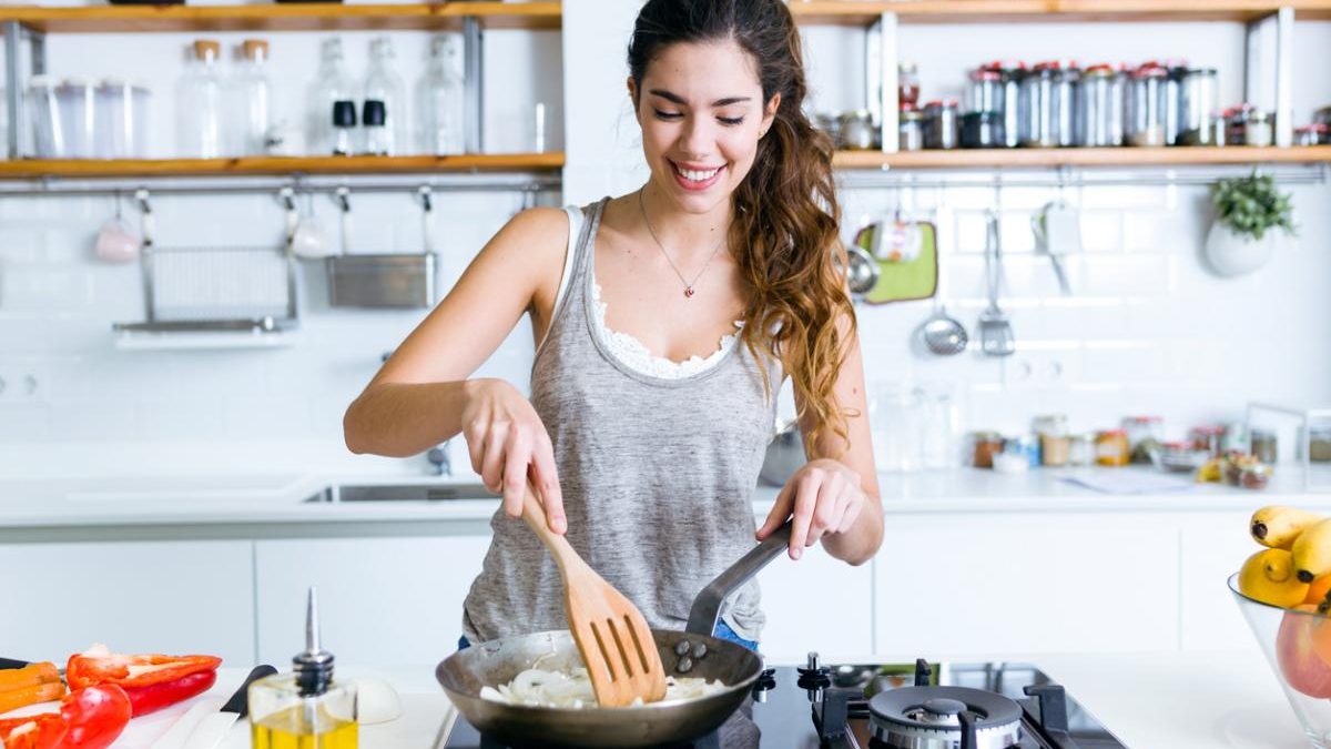 Young woman frying onion into the pan in the kitchen.