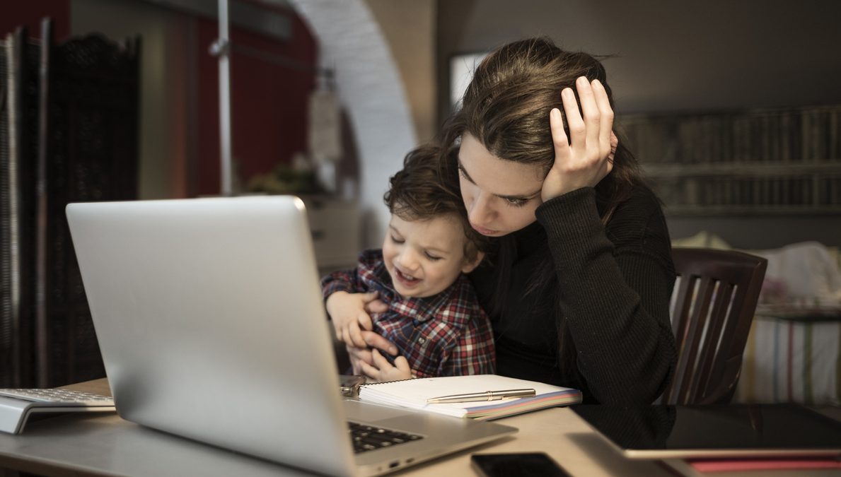 Worried woman working at home and holding her crying little son