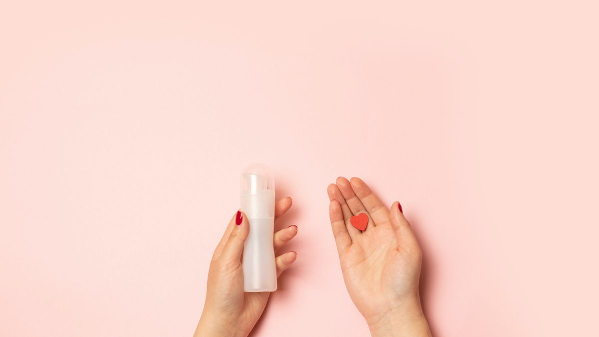 Womens hands hold intimate grease and a red heart shape on a pink background Womens hands hold intimate grease and a red heart shape on a pink background