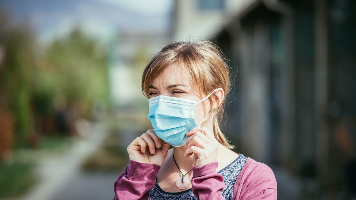 Flue and corona safety concept. Woman putting on face mask to protect herself, outdoors