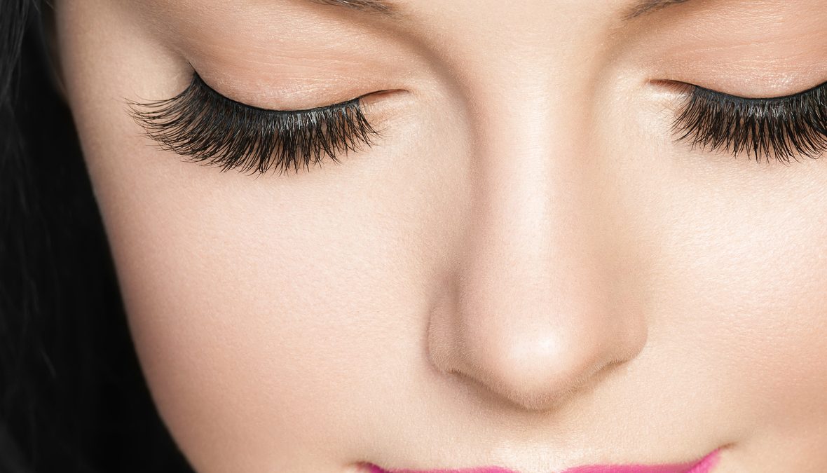 Beautiful brunette woman with eyelashes extension and long brunette curly hairstyle pink lipstick.