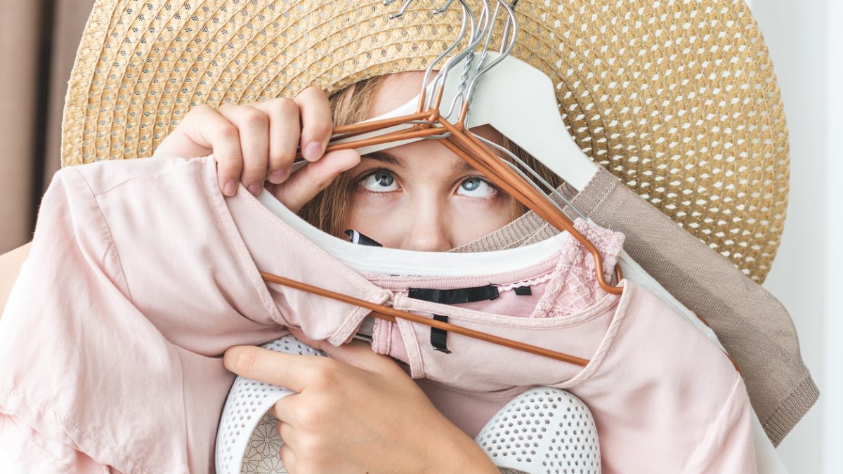 Woman can not choose which clothes pack for travel. Clothing, fashion, style and people concept - woman choosing clothes at home wardrobe.