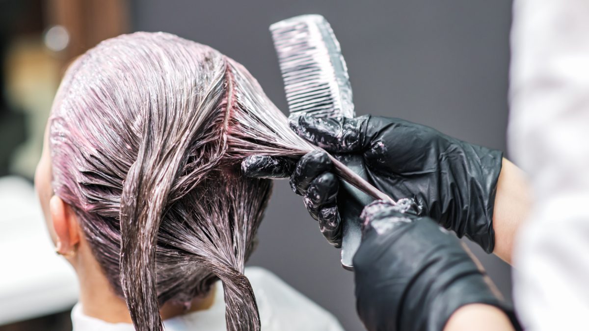 Close up of hairdresser hands is coloring woman's hair in black gloves.