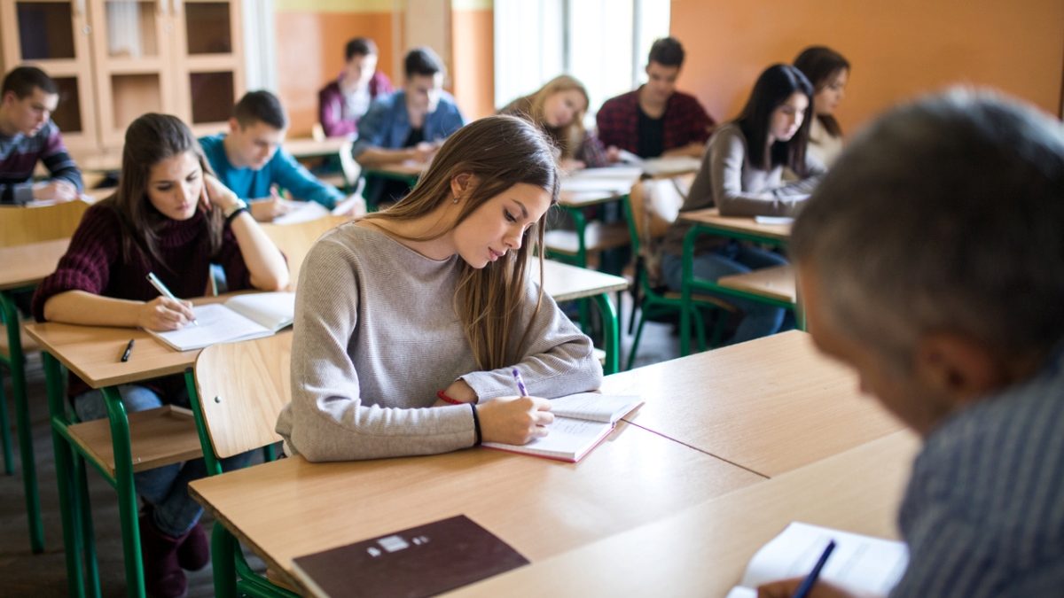 Large group of students sitting in the classroom and writing a test.