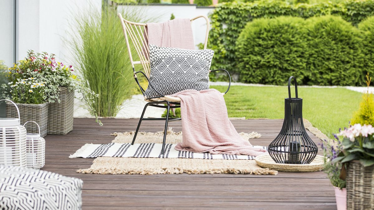 Real photo of a white pillow and pink blanket on a rattan chair standing in the garden of a luxurious house