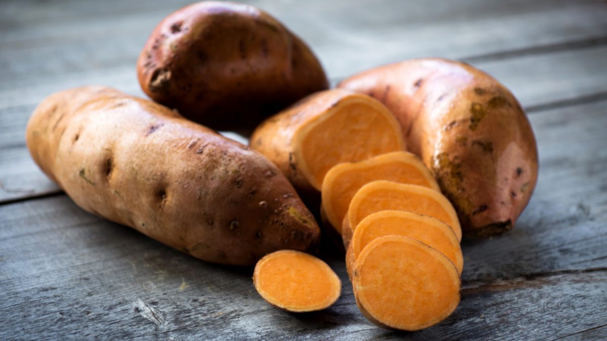 Raw sweet potatoes on wooden background closeup