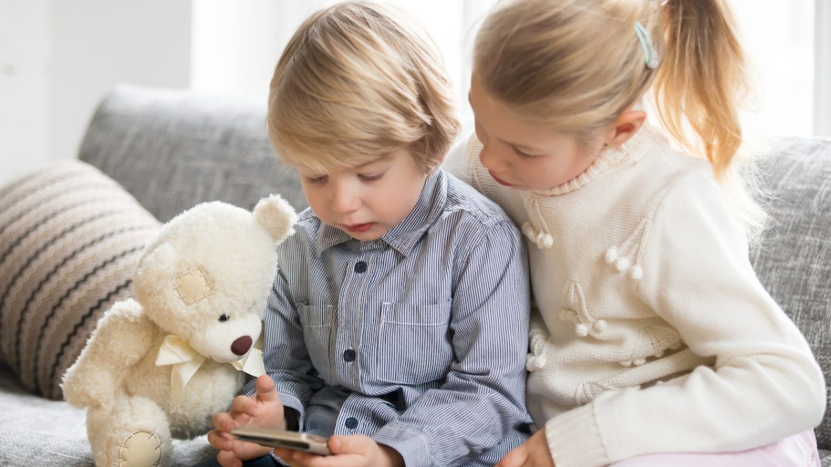 KIds boy and girl using smartphone together sitting on sofa KIds boy and girl using smartphone together sitting on sofa
